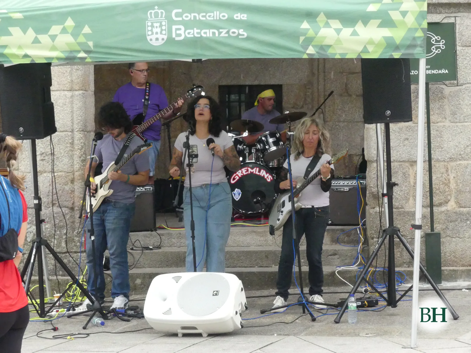 Banda de rock tocando bajo una carpa del Concello de Betanzos en los soportales, con cantante, guitarristas y batería.